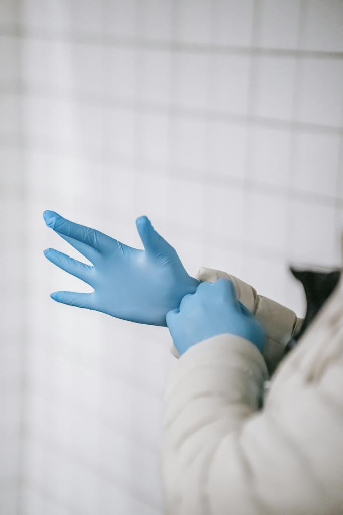 Crop anonymous person wearing warm clothes putting on latex gloves while standing in public place hallway